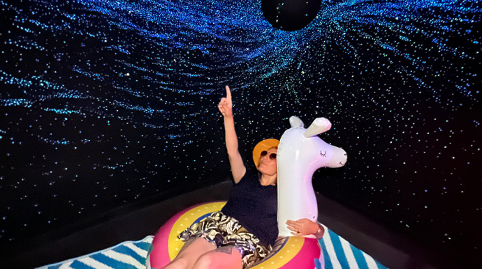 Anaïs, médiatrice conférencière au Planétarium, sur une bouée gonflable, sous un trou noir et les étoiles