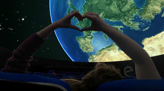 deux personnes dans le planétarium qui font un coeur avec leurs mains devant une projetion de la planète Terre