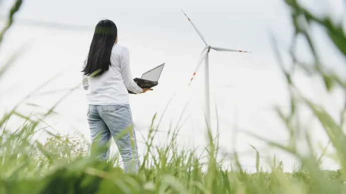 photo d'une femme dans un champs d'herbe, regardant une éolienne