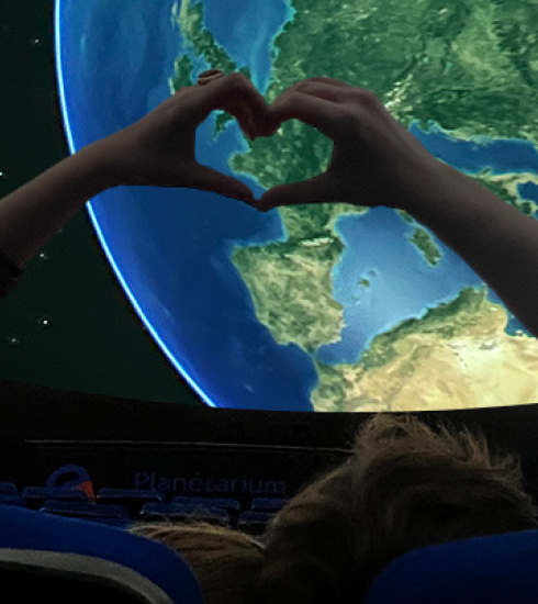 deux personnes dans le planétarium qui font un coeur avec leurs mains devant une projetion de la planète Terre