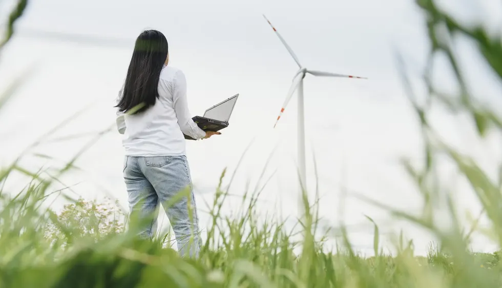 photo d'une femme dans un champs d'herbe, regardant une éolienne